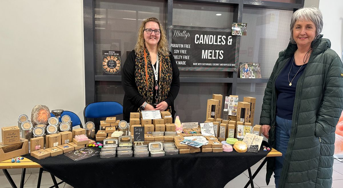 One person standing beside and another person standing behind a table selling candle and melts products